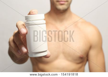 Muscular man holding drugs in bottle, closeup