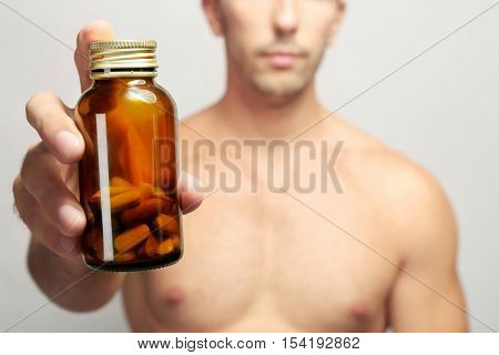 Muscular man holding drugs in bottle, closeup