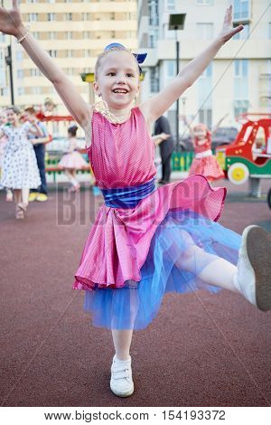 Little girl in dance suit dances at playground in courtyard.