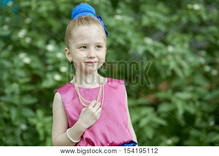 Half-length portrait of little girl standing outdoor against green bushes.
