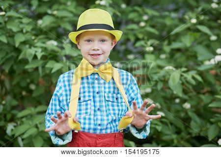 Half-length portrait of little boy in dance suit pulling off braces with thumbs.
