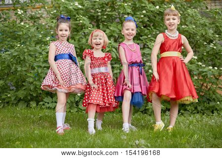 Four smiling little girls dressed in dancing suits pose at grassy lawn.