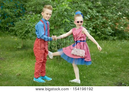 Boy and girl dressed in red and blue costumes dance at grassy lawn.