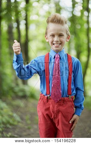 Portrait of grinning boy showing thumb up in summer park.