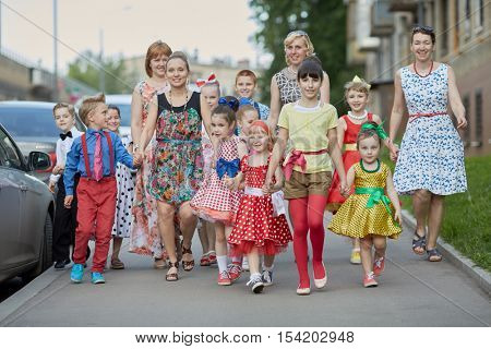 Group of eleven children and four woman walks down street.