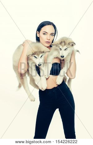 pretty sexy brunette woman with long straight hair fashion makeup in black bra holding cute little dogs of husky isolated on beige background