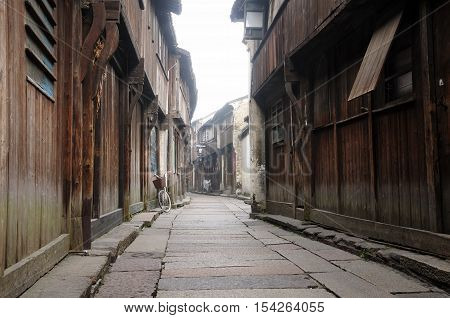Wooden weathered buildings lining a narrow walkway in tongxiang wuzhen scenic town east view in Zhejiang province China in the early morning mist.