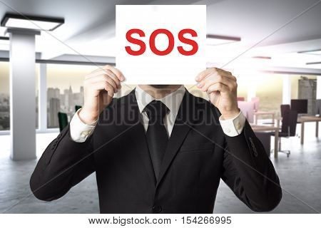 businessman in office hiding face behind sign sos