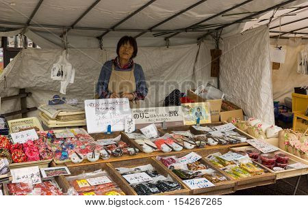 Takayama Japan - September 24 2016: Middle aged lady who is a vendor on the public morning market in front of the Jinya Hall promotes pickled and other merchandise. Combination of colors.