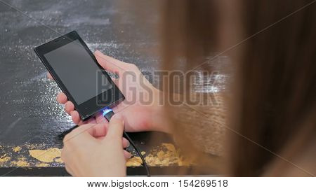 Woman's hand plugging black lightning charging cable into smartphone - USB data cable connecting on modern gadget