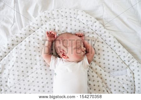 Cute little newborn baby boy lying on bed, sleeping, hands up. Close up.