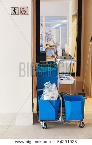 cart with cleaning supplies cleaners near a public toilet. Buckets and cleaners and rags.