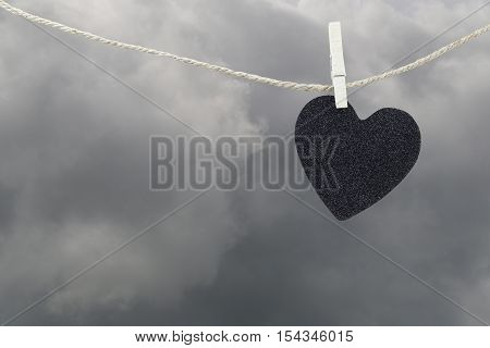 Black Heart paper hanging on a brown hemp rope on rain clouds backgroundConcepts about unrequited love and heartbreak.