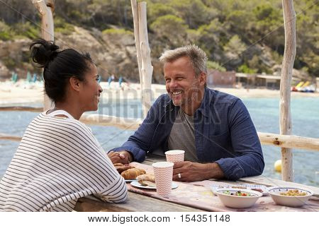 Middle aged couple smiling across a table by the sea, Ibiza