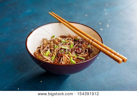 Stir fry noodles yakisoba with beef in a bowl on a blue background. Asian cuisine meal.