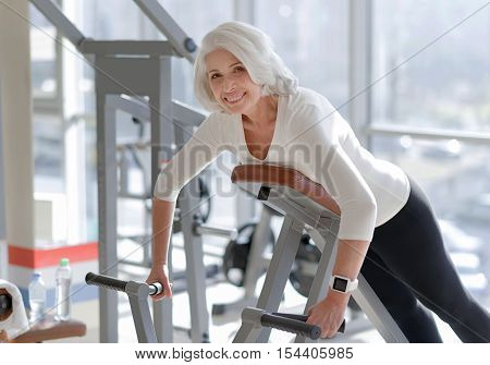 Inspiring workout. Senior athletic fit woman smiling and doing exercise for the back muscles while working out in the gym.