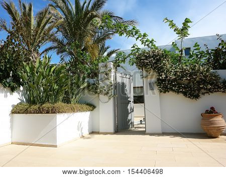 HERAKLION CRETE GREECE - MAY 13 2014: The blue sky and open door on the terrain of villa with flowers palms and amphora in luxury class hotel on the Mediterranean coast of Crete May 13 2014 Greece.