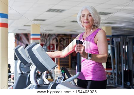Just know what I want. Beautiful inspired senior woman listening to music and exercising on exercise bike while spending time in a gym.