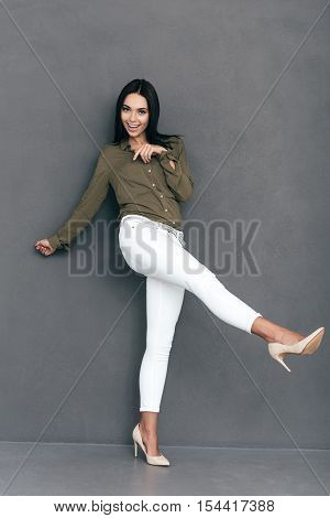 Playful and beautiful. Full lenght of attractive young woman in smart casual wear posing against grey background and looking happy