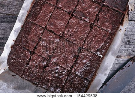 Homemade chocolate brownies cuted by squares on dark wood background woth baking sheet and pan. Top view.