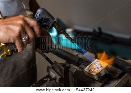 Close-up of Goldsmith hands melting Silver to liquid state in crucible with blowtorch
