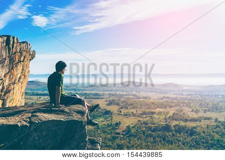 Young Man In Green Sportswear Is Sitting On Cliff's Edge