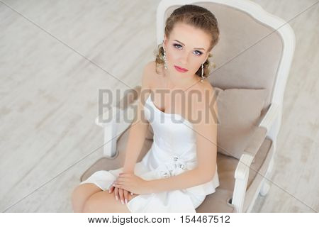 A girl sits in a chair in a white dress posing in the photo