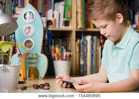 School kid boy sitting at his table and watching tablet pc at home indoors. Child with tablet computer in his room. Studying with tablet computer.