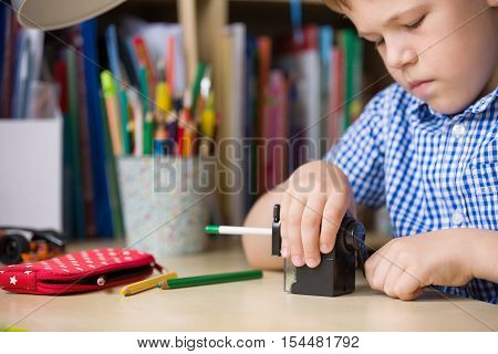 Portrait of cute school boy sitting at his desk and sharpening pencils. Child preparing for lessons.