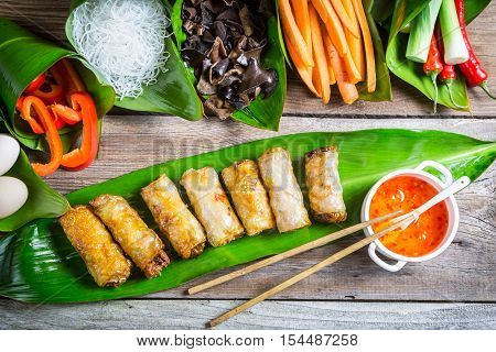 Fried spring rolls surrounded by ingredients on old wooden table
