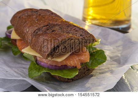 Sandwich with rye bread salmon and vegetables and glass of beer. Selective focus.