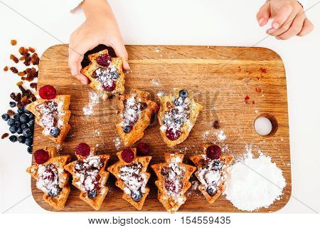 Child take berry cake from board, flat lay. Top view on platter with set of sweet cookies and kid hand treating on. Sweet-tooth, little monkey, pastry eating concept