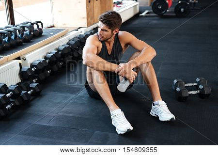Atletic man sitting down in gym and looking away
