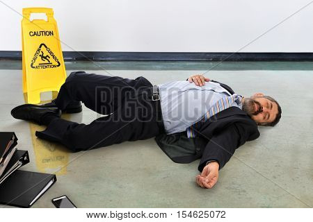 Hispanic businessman laying injured on the floor next to caution sign