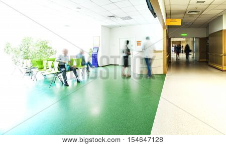 View of the registration desk, waiting area and a corridor in modern hospital with blurred figures of patients with a copy space.