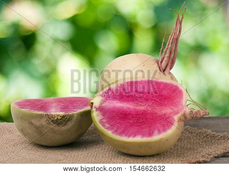 One whole and sliced watermelon radish on a wooden table with blurred garden background.