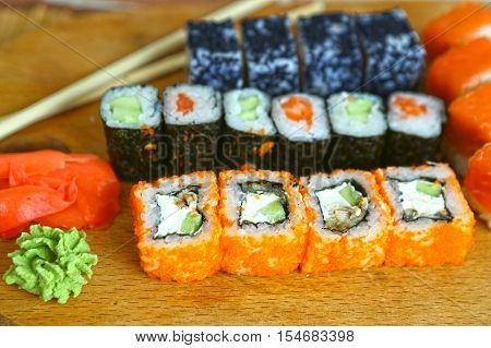 japanese sushi roll set in row on wooden kitchen board with sticks vasabi mustard and ginger close up photo
