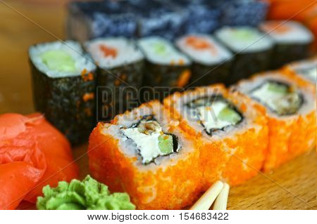 japanese sushi roll set in row on wooden kitchen board with sticks vasabi mustard and ginger close up photo