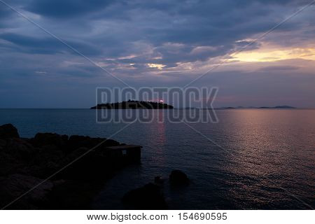 Dark silhouettes of island and coast land after sunset in blue sea under cloudy sky on tranquil evening seascape