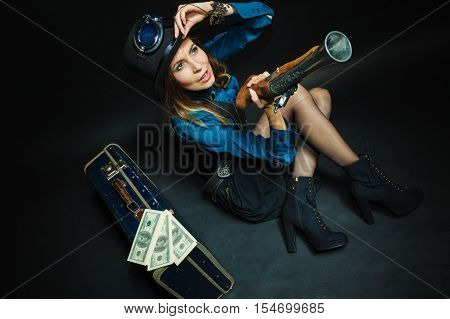 Fashionable subculture weapon concept. Steampunk girl with cash. Young gorgeous lady in victorian fashion lying on floor with banknotes briefcase and blunderbuss.