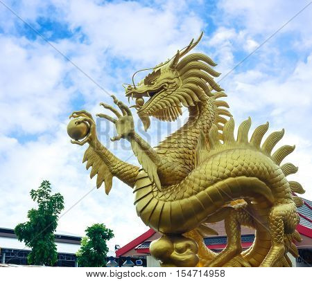 Golden dragon sculpture holding a crystal ball and a beautiful sky.