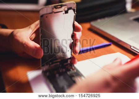 A close-up process of disassemble and dismantle modern mobile phone smartphone with broken shattered display glass and changing details at home