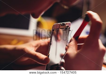A close-up process of disassemble and dismantle modern mobile phone smartphone with broken shattered display glass and changing details at home