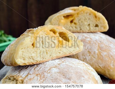 Ciabatta with cheese stuffing - freshly baked Italian white bread on a dark wooden background. For the preparation of sandwiches.