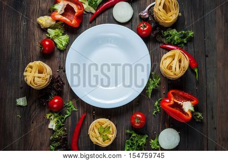Ingredients for cooking spagetti cherry tomatoes pepper around a white plate place text frame on wooden rustic background top view.