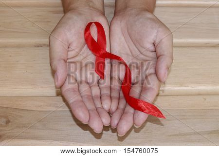 The symbolic conception of the world day of fight against AIDS. The red ribbon in the hands of a young woman on wooden background.