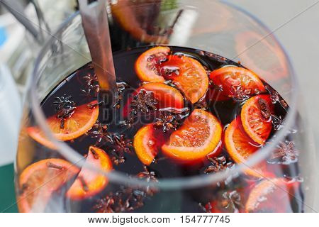 Making hot alcohol, mulled wine for sale at country fair. Glintwine from red wine with citrus and cloves in big glass, mixed with soup ladle. Closeup