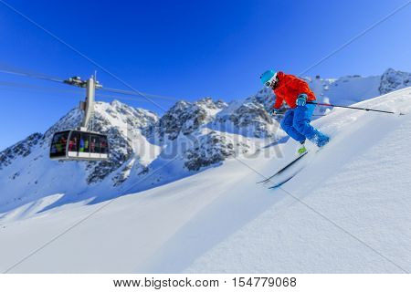 Skier skiing downhill in high mountains in fresh powder snow. Snow mountain range and cable railway in background. Mt Fort Peak Alps region Switzerland.