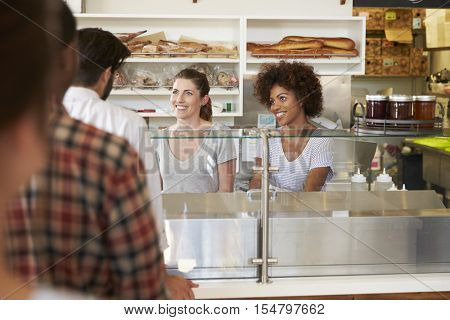 A queue of customers served by two women at a sandwich bar