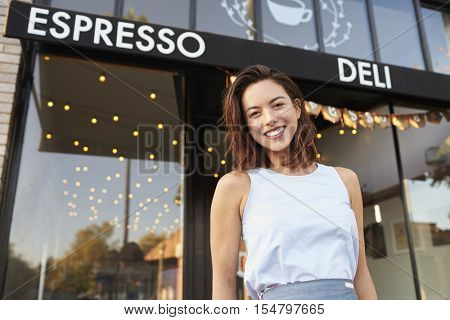 Young woman business owner standing outside cafe shopfront